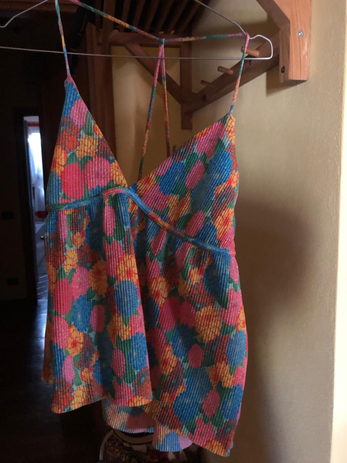 Strappy top with colourful floral print in shades of pink, blue and yellow, hanging on a hanger inside a room.
