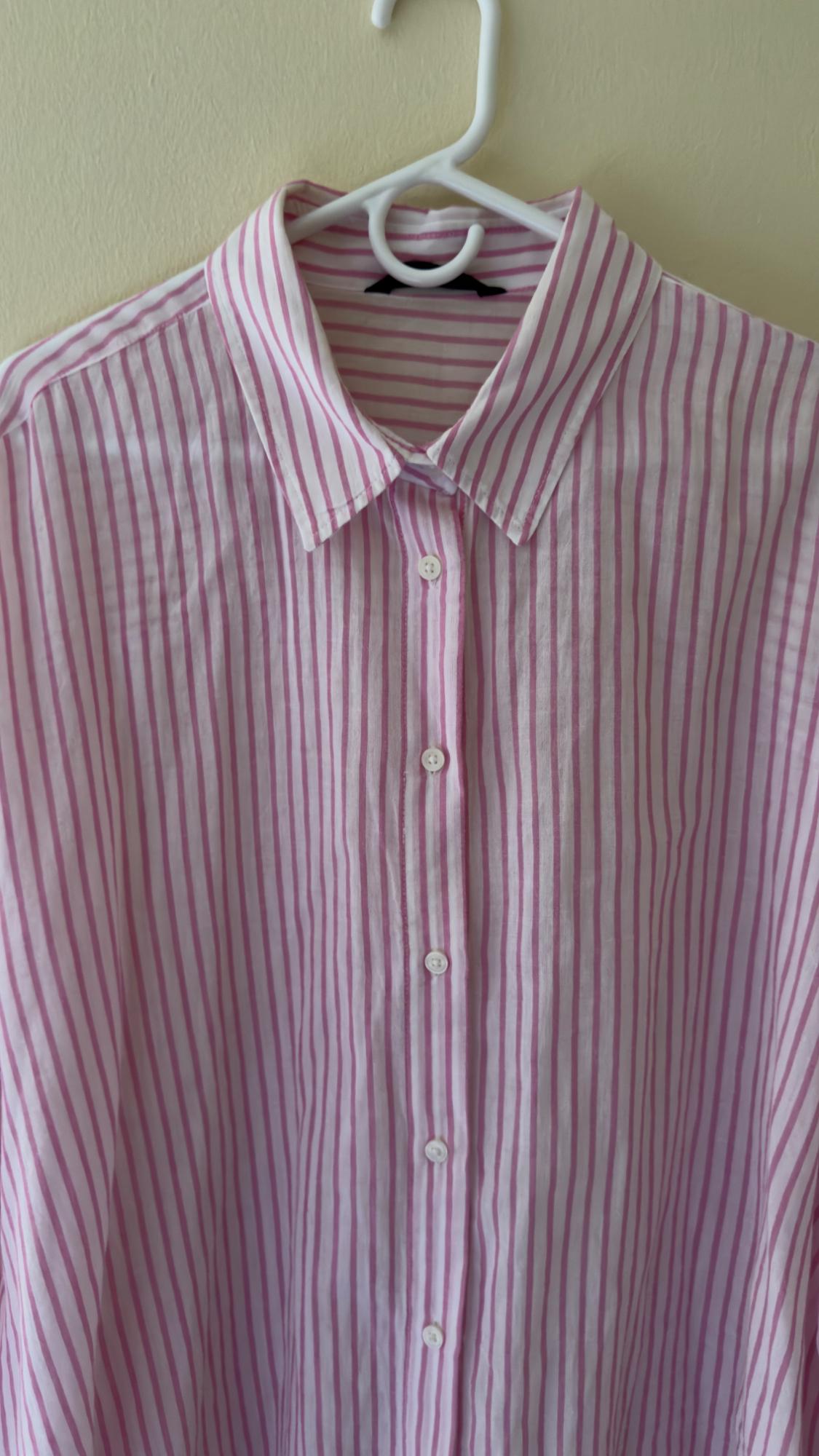 Pink and white vertical striped shirt hanging on a white hanger against a beige wall.