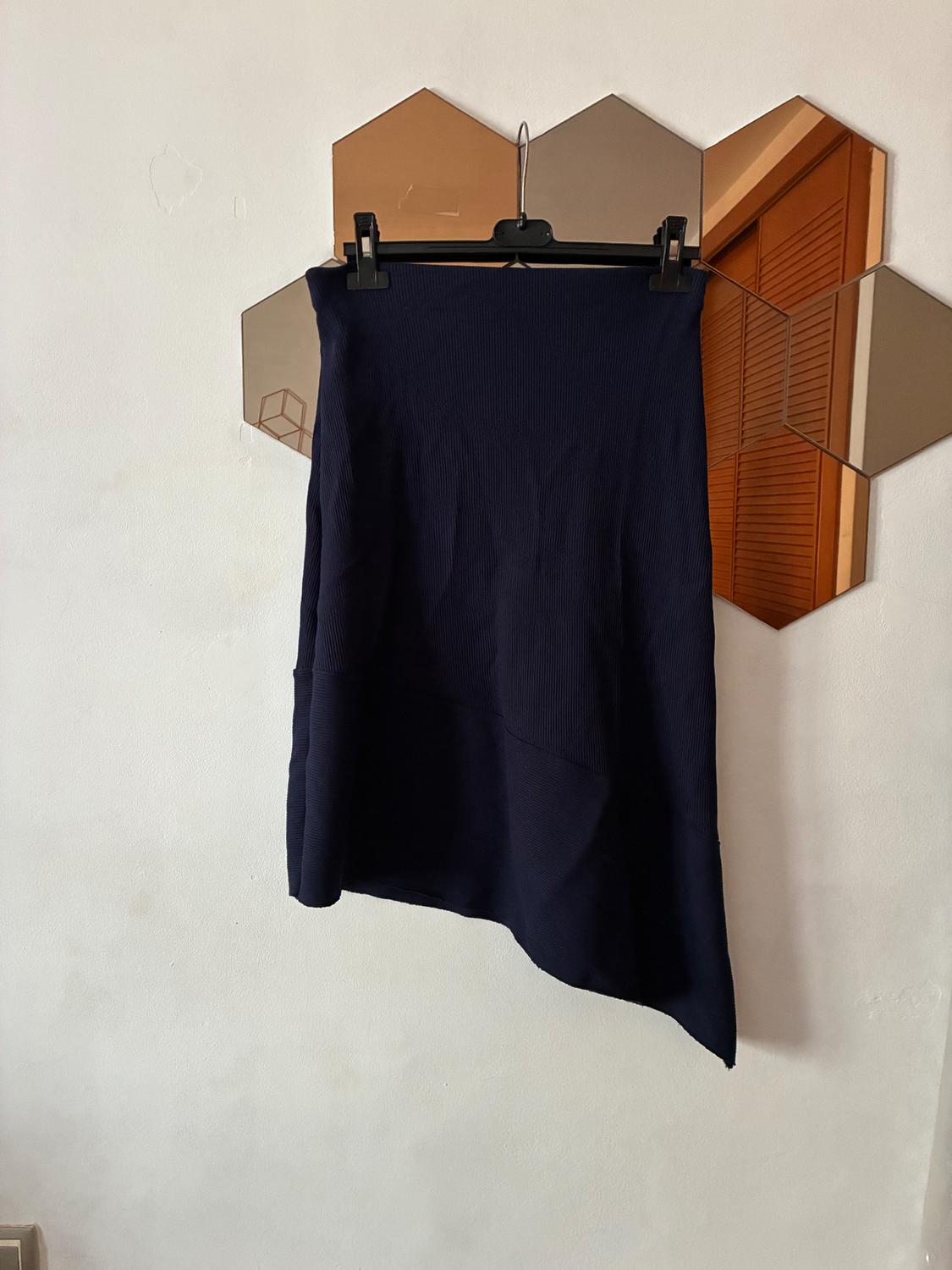 Black asymmetrical skirt hanging on a hanger against a background of hexagonal mirrors on the white wall.