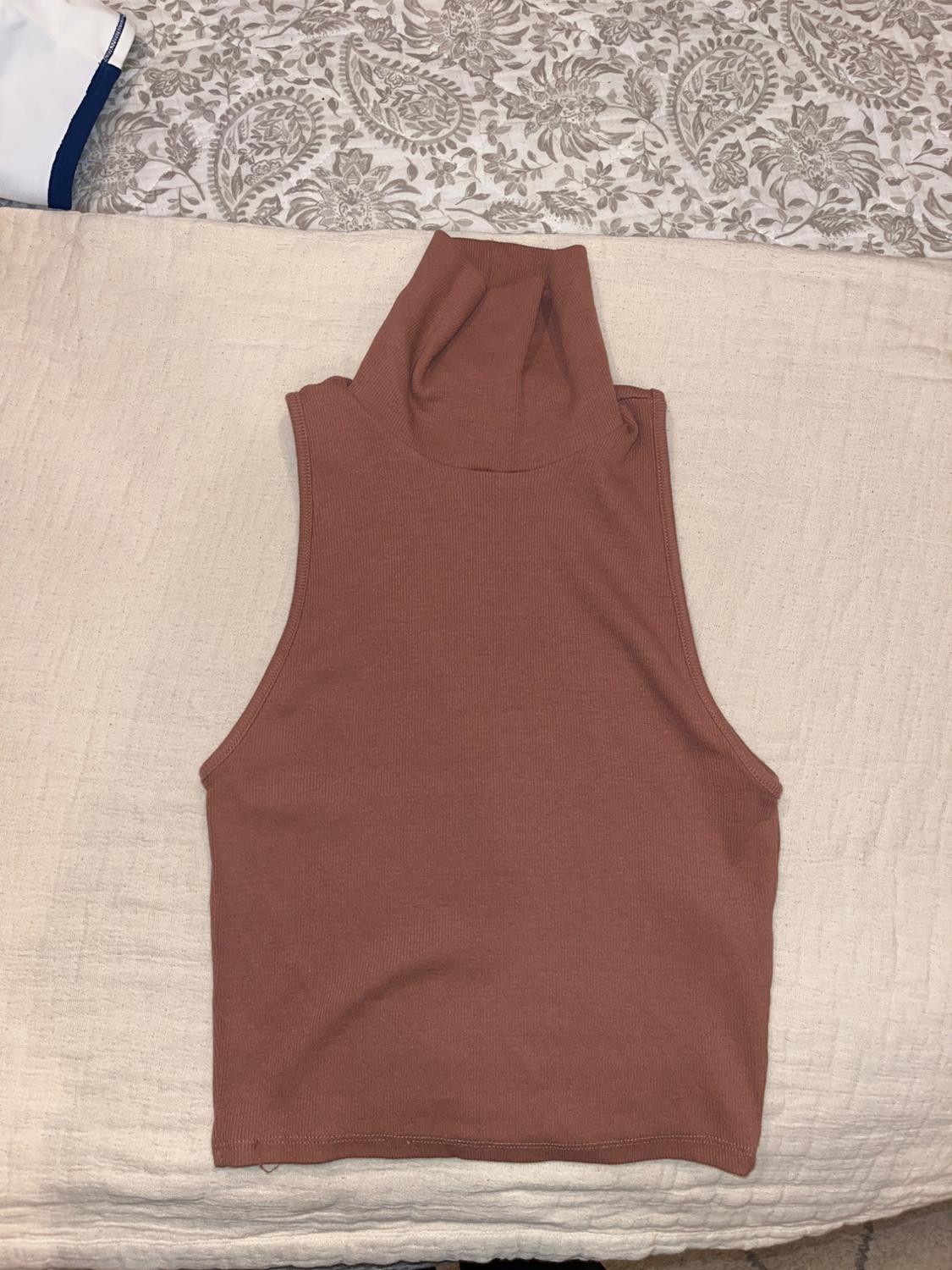 Brown sleeveless top with a high neck, on a beige quilt and grey-toned patterned fabric background.