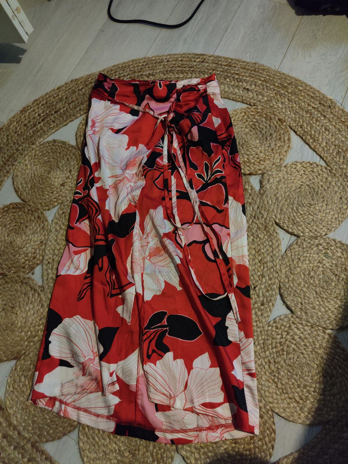 Red long skirt with black and white floral print, over a braided jute rug on a light wooden floor.