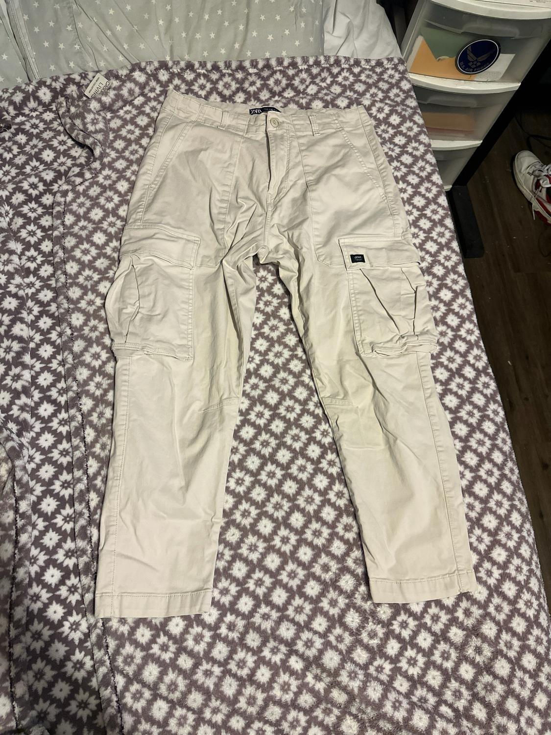 Beige cargo pants spread over a star-print bedspread. They have side pockets and a Zara label.
