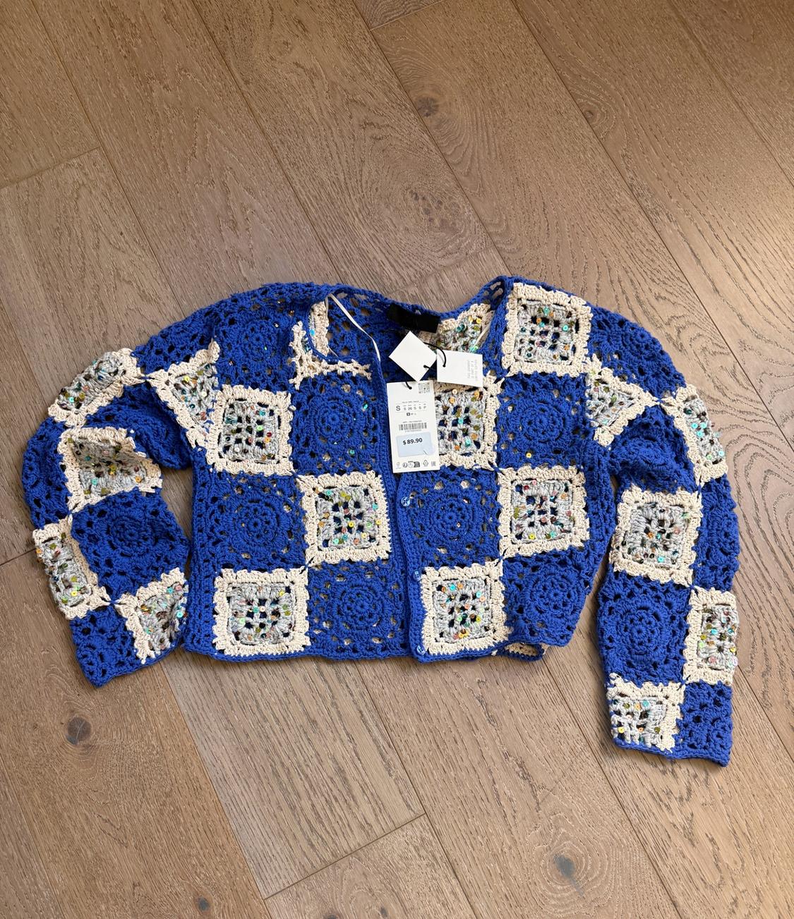 Blue and ecru crochet cardigan with a plaid pattern on a wooden floor. Tag with the text $89.90.