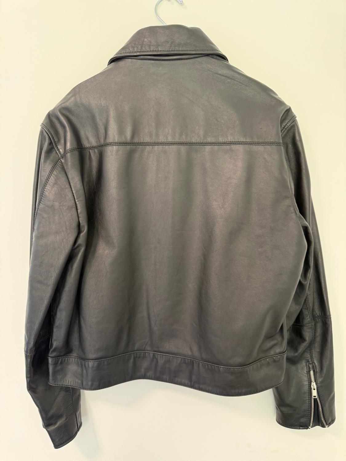 Rear view of a black leather jacket hanging on a hanger against a light background, showing a zipper detail on the sleeve.