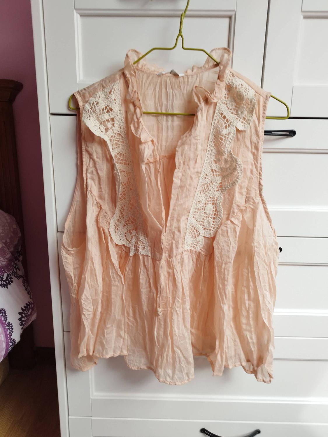 Peach sleeveless blouse with lace details hanging on a green hanger in front of a white wardrobe.