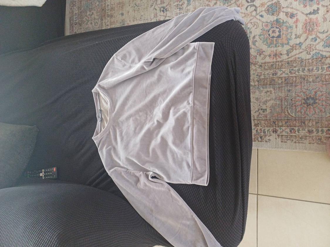 Light grey long-sleeved sweatshirt on a black sofa, with a remote control next to it and a decorative rug in the background.