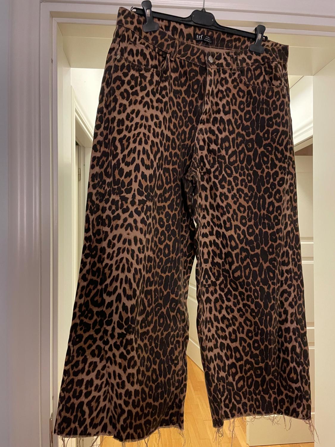 Animal print trousers hanging on a black hanger, with a frayed hem, in an interior with white walls.