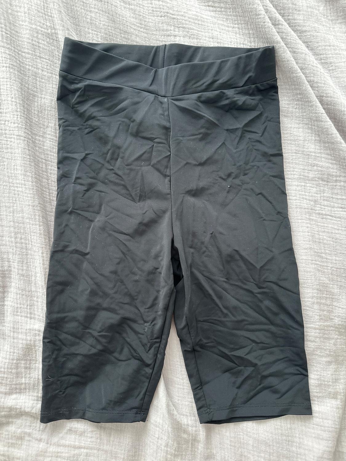 Black crinkled shorts on a light grey fabric surface.