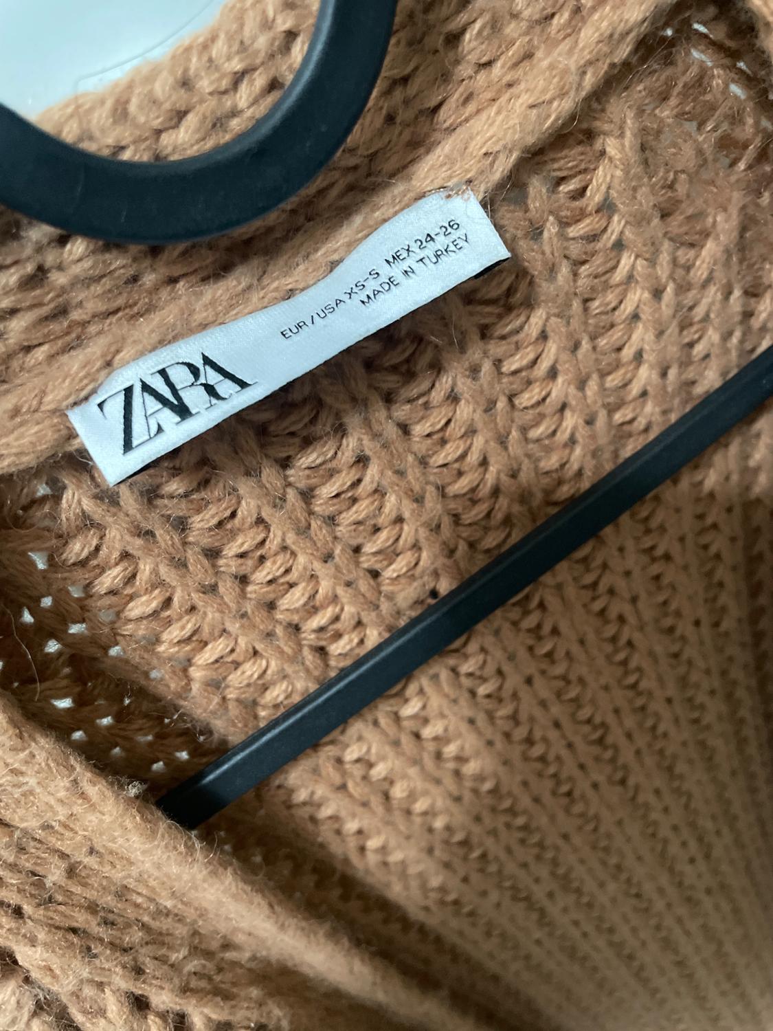 Label of a beige knitted jumper on a black hanger. Visible text: "ZARA, EUR/USA: XS-S, MEX: 24-26, MADE IN TURKEY".