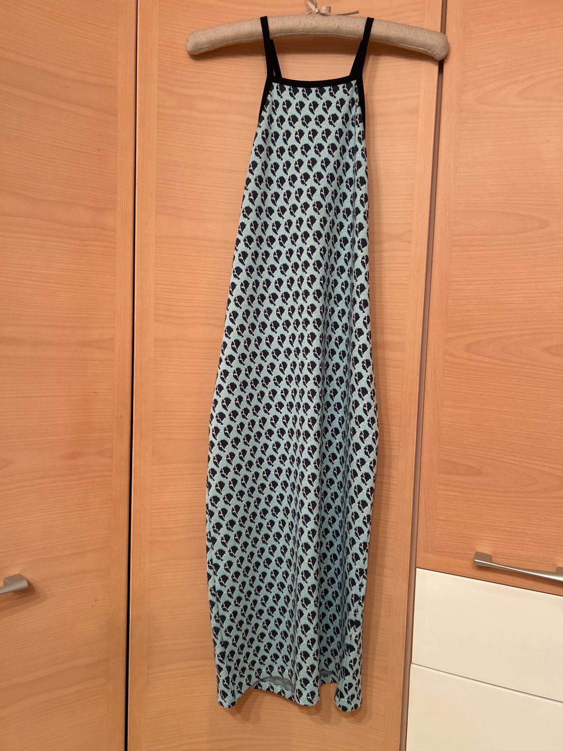Light blue long dress with a black pattern, hanging on a wooden hanger, against a background of light wooden wardrobe doors.
