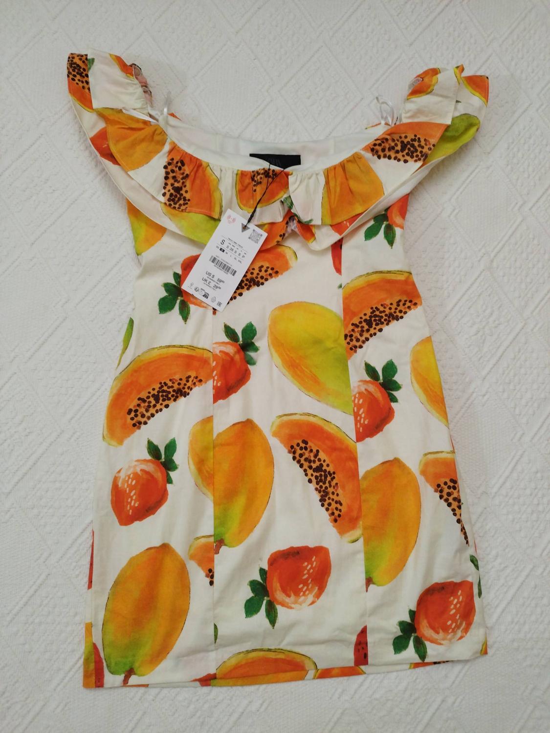 White dress with a papaya and mango print, frilled neckline, on a textured white surface. Price tag visible.