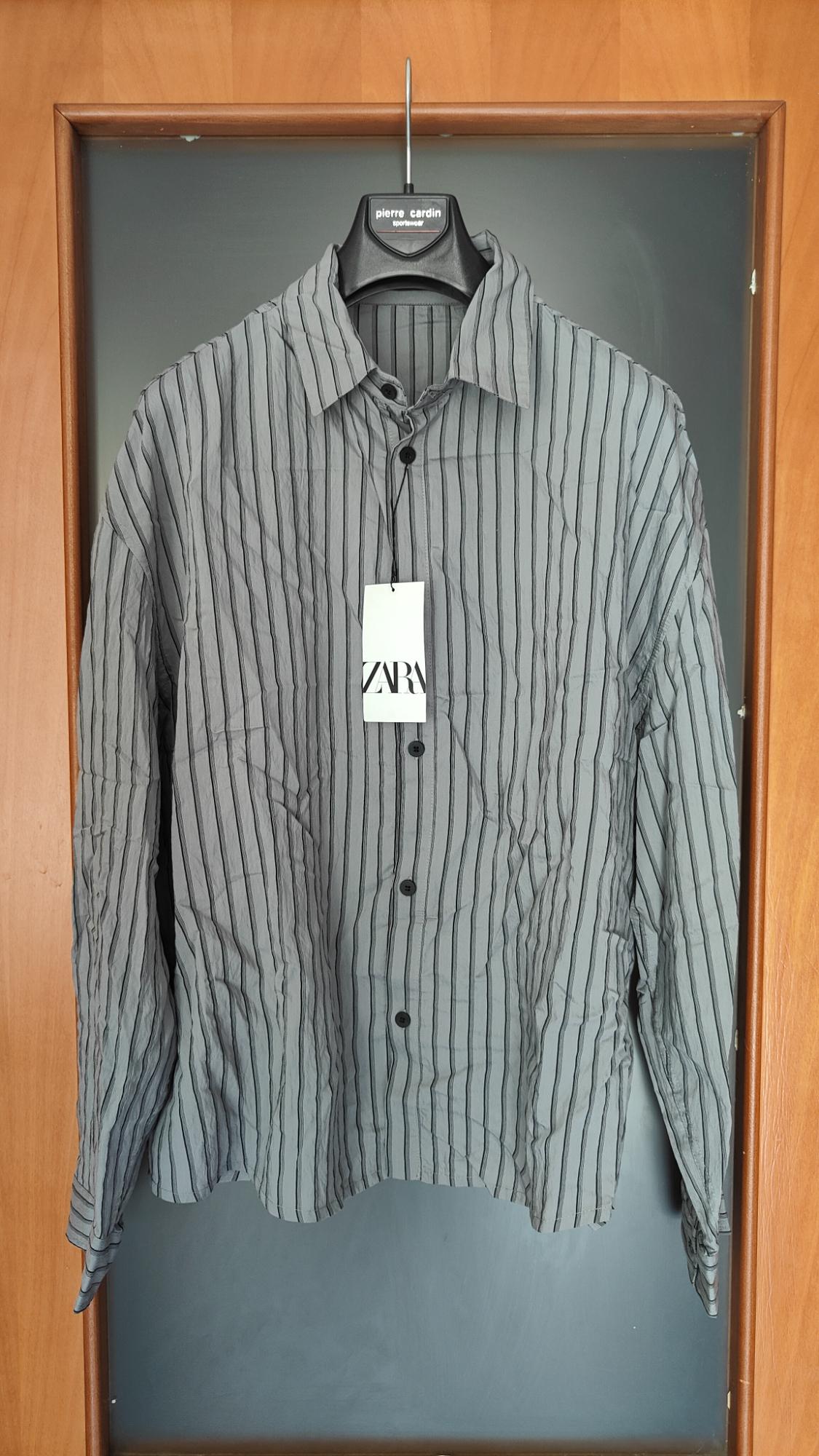 Grey shirt with black stripes hanging on a hanger. Texts: "pierre cardin sportswear" and "ZARA".