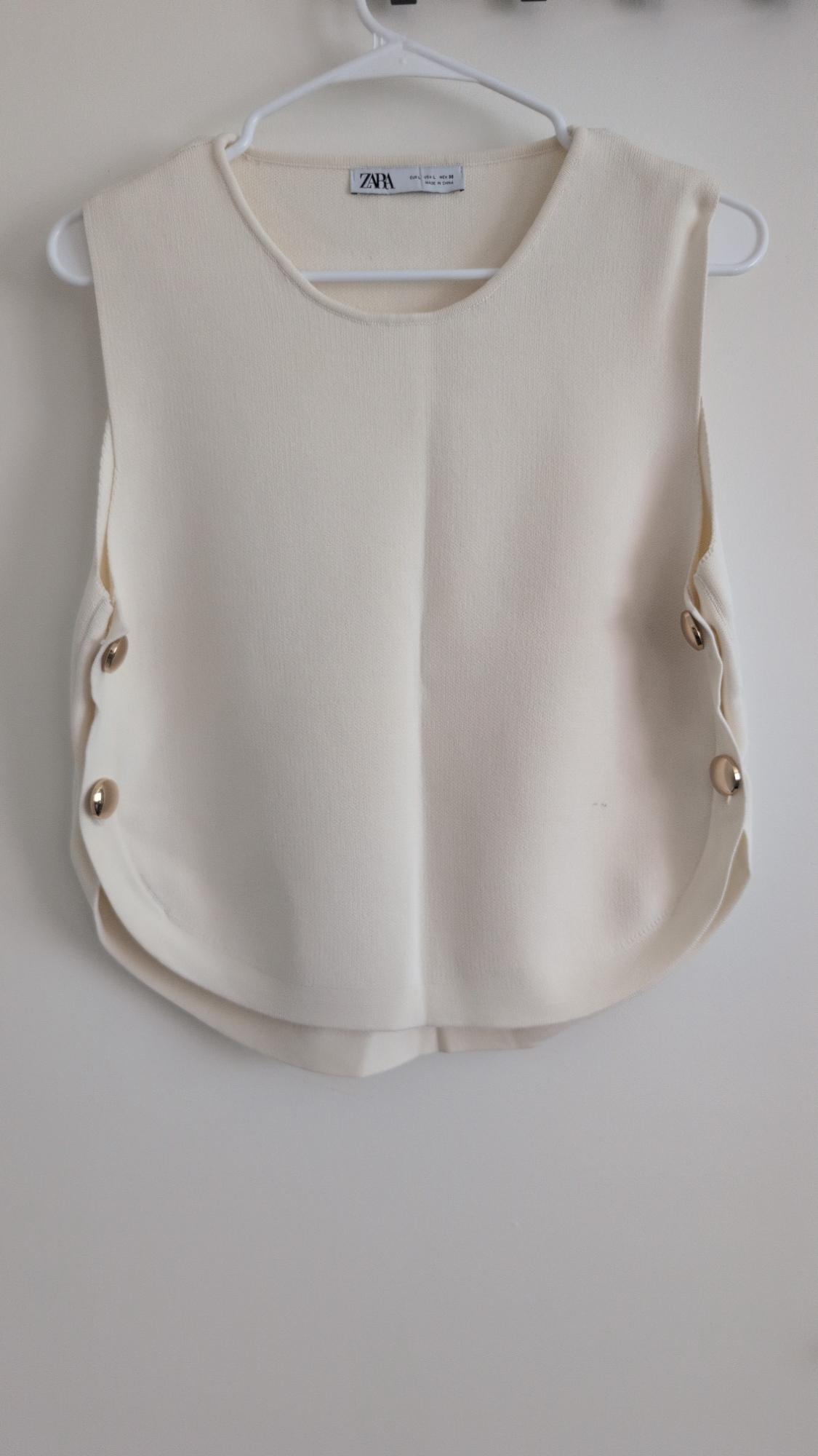 Cream sleeveless top on a white hanger. Open sides with gold buttons. Label: ZARA EUR L USA L MEX 30 MADE IN CHINA.