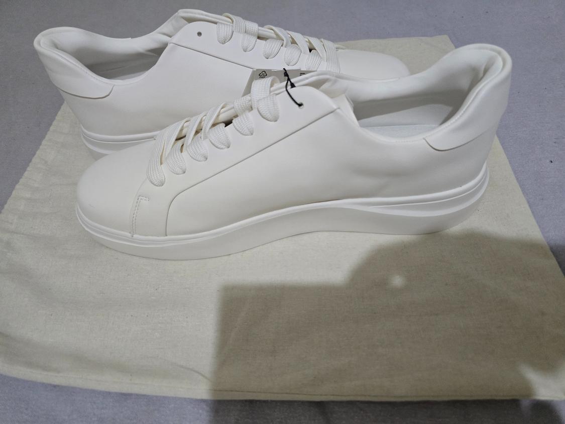 White trainers with laces resting on a light-coloured canvas bag on a grey surface.