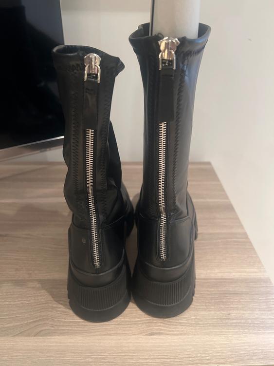 Black boots with silver zips at the back, on a light wooden surface. Black and white background.