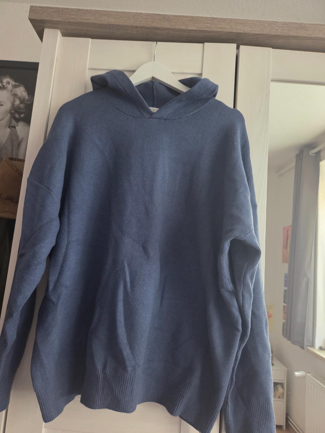 Blue knitted hoodie hanging in a white wardrobe. In the background, there is a photograph and a mirror reflecting the room.