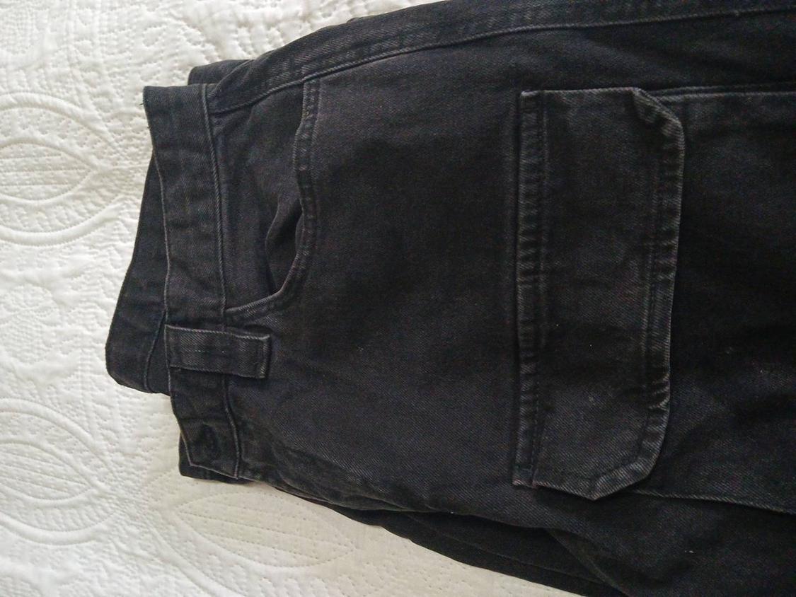 Black trousers folded on a white quilt with a textured design. Back pocket visible.