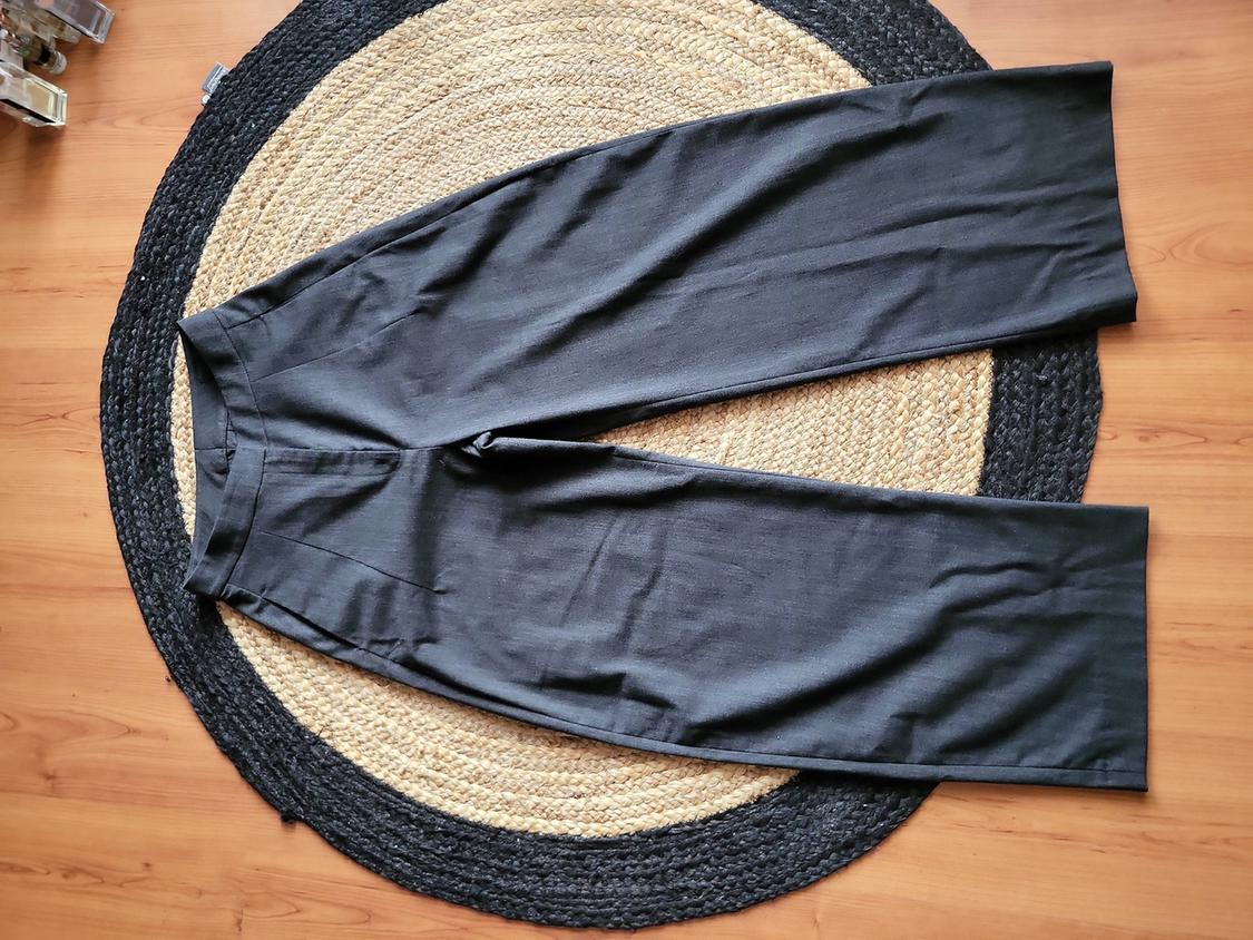 Black wide-leg trousers on a round jute rug on a light wooden floor.