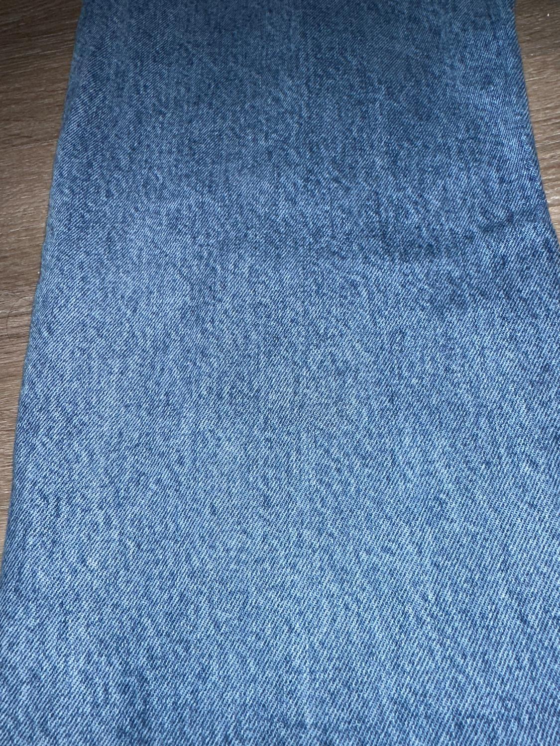 Blue denim fabric on a brown wooden surface. The texture of the fabric is clearly visible.