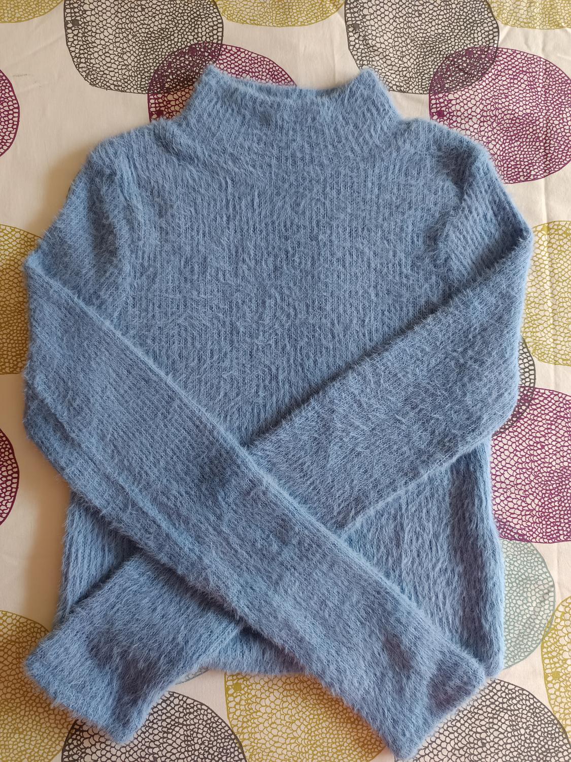 Blue roll-neck, soft-textured jumper on a bedspread with a circle pattern in beige, red, and yellow tones.