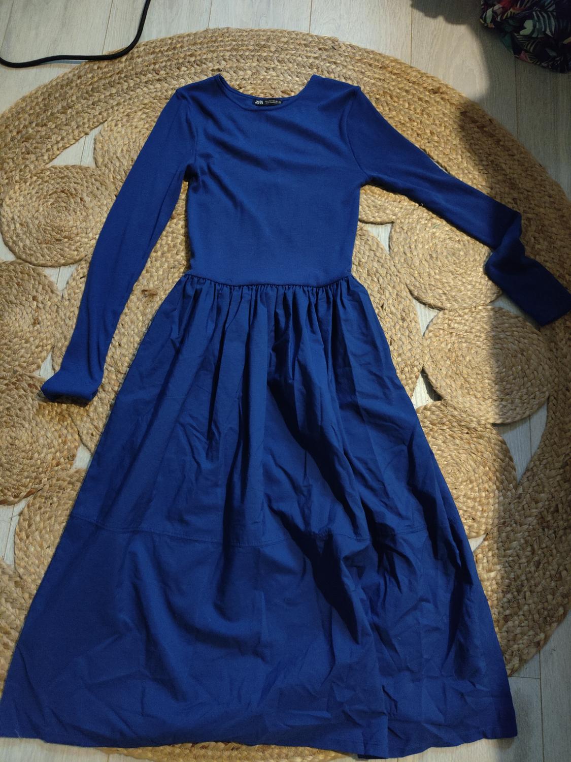 Long-sleeved blue dress on braided jute rug on light wooden floor.