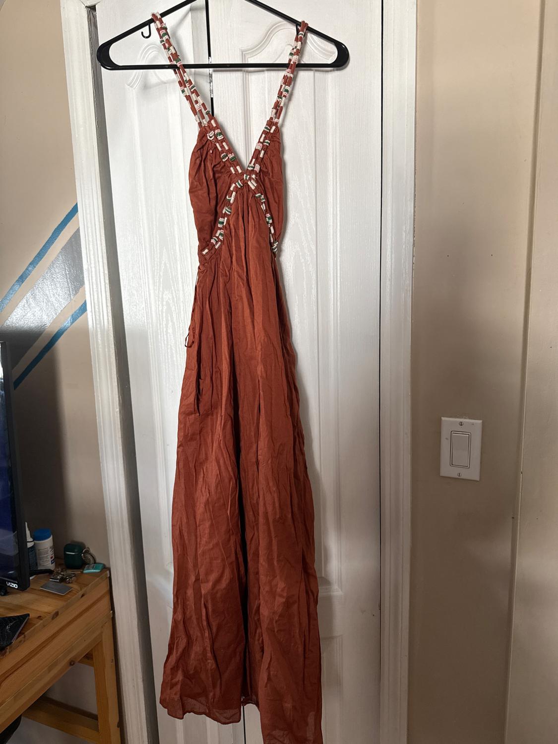 Long brown dress with braided straps hanging on a black hanger over a white door. Indoor setting.