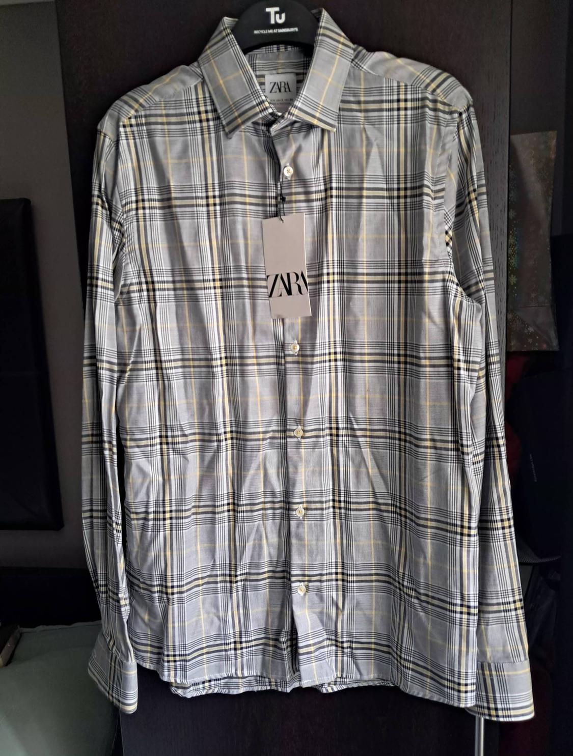 Grey and yellow checked shirt hanging on a black hanger with a ZARA tag. Dark background.