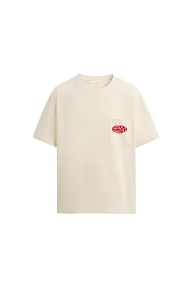 Front view of a cream-colored t-shirt with a pocket and red print on the chest.