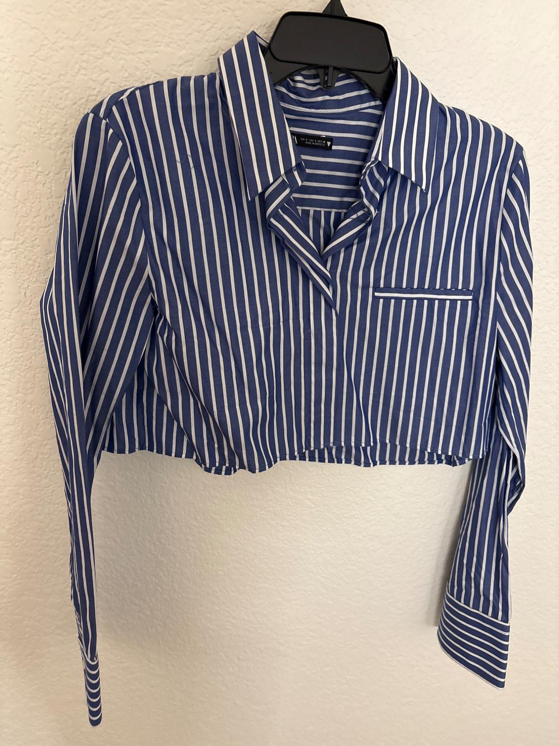 Blue and white striped crop top hanging on a black hanger against a white wall.