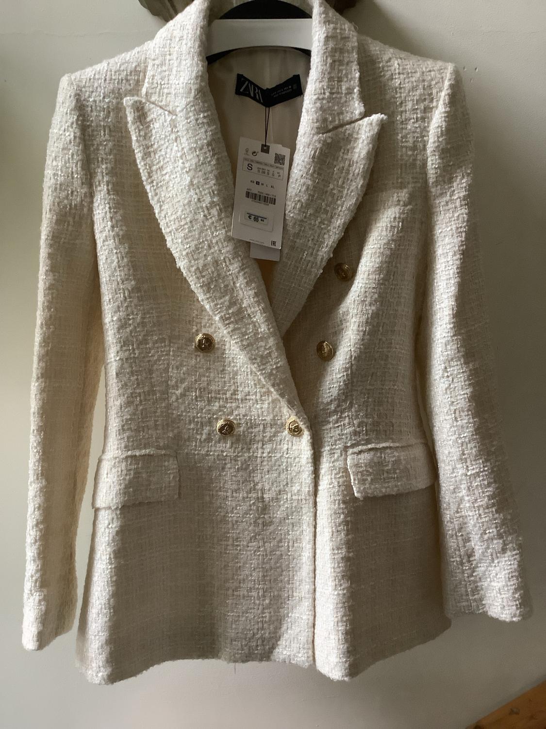 Double-breasted Ecru blazer with texture and gold buttons, hanging on a hanger. Label with the text ZARA.