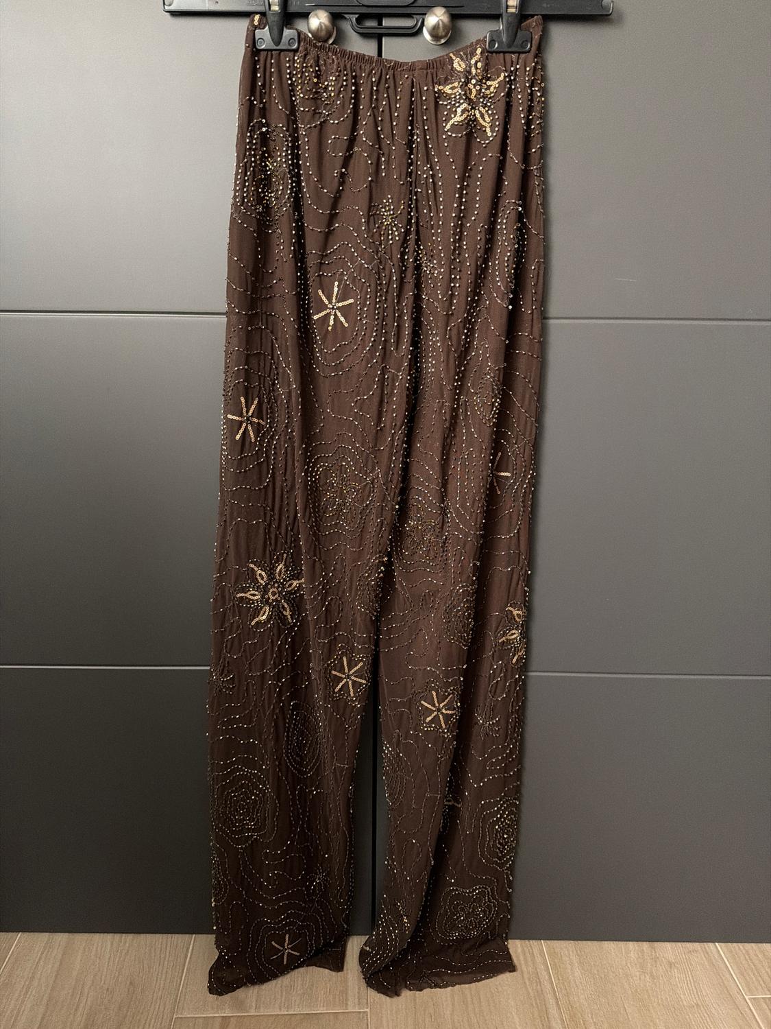 Brown trousers hung with gold embroidered details and star patterns, on a dark grey background.