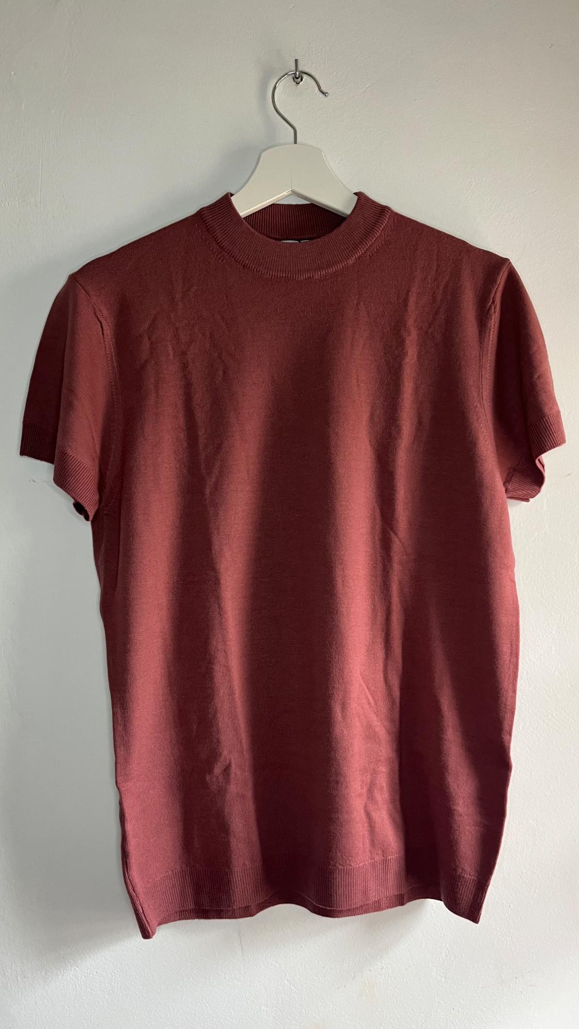 Brown short-sleeved t-shirt hanging on a white hanger against a white wall.