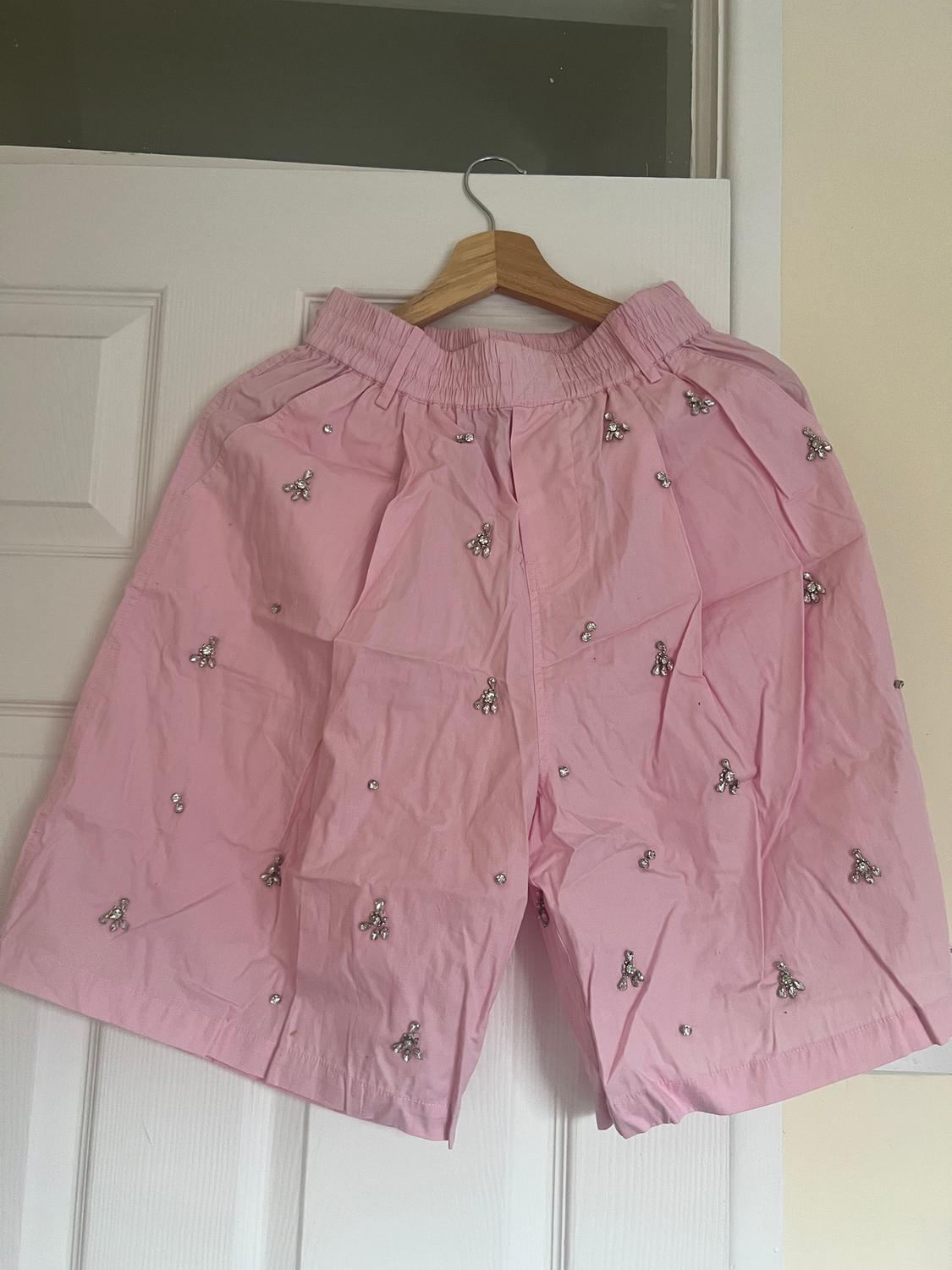 Pink shorts with sparkly embellishments hanging on a wooden hanger over a white door.
