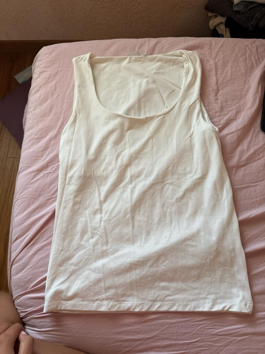 Basic white vest top laid out on a rumpled pink sheet. Casual, relaxed style, viewed from above.