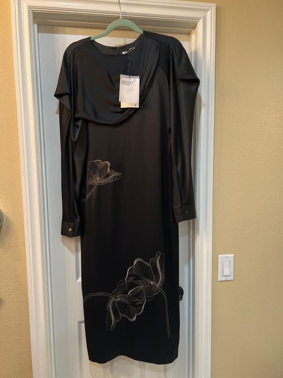 Long-sleeved black dress with a floral design on the bottom, hanging on a white door. Label visible on the collar.