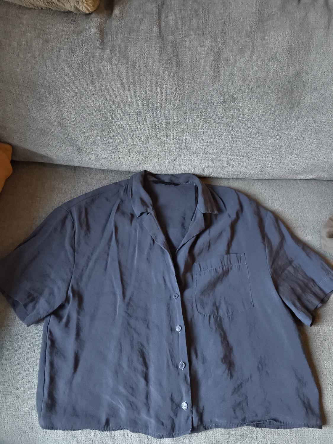 Blue, short-sleeved, button-up shirt with a chest pocket, placed on a grey sofa.