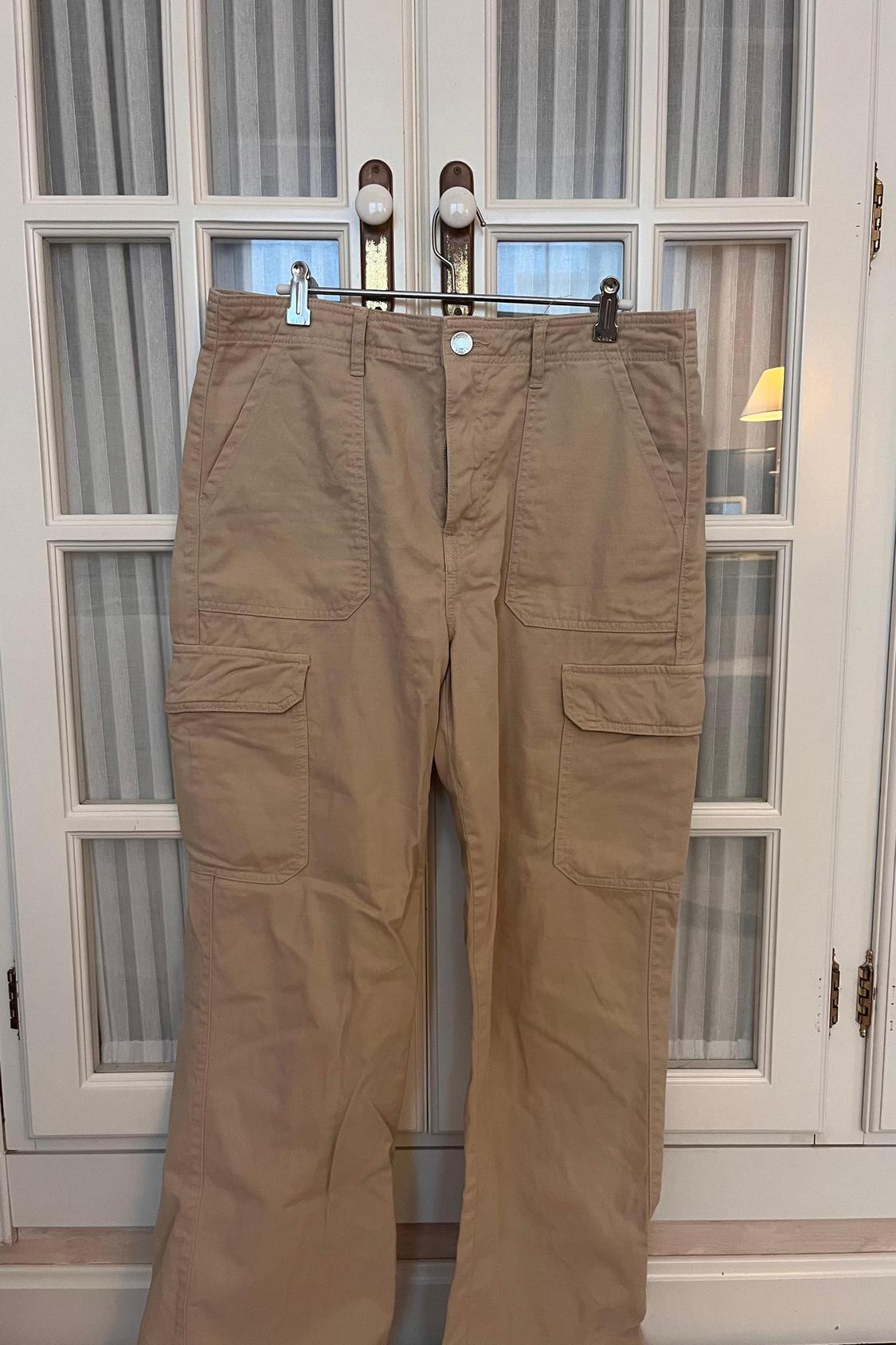 Front view of beige cargo trousers with side and front flap pockets.