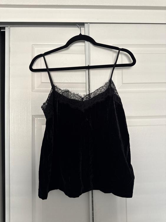Black spaghetti strap top with lace hanging on a black hanger in front of a white door.