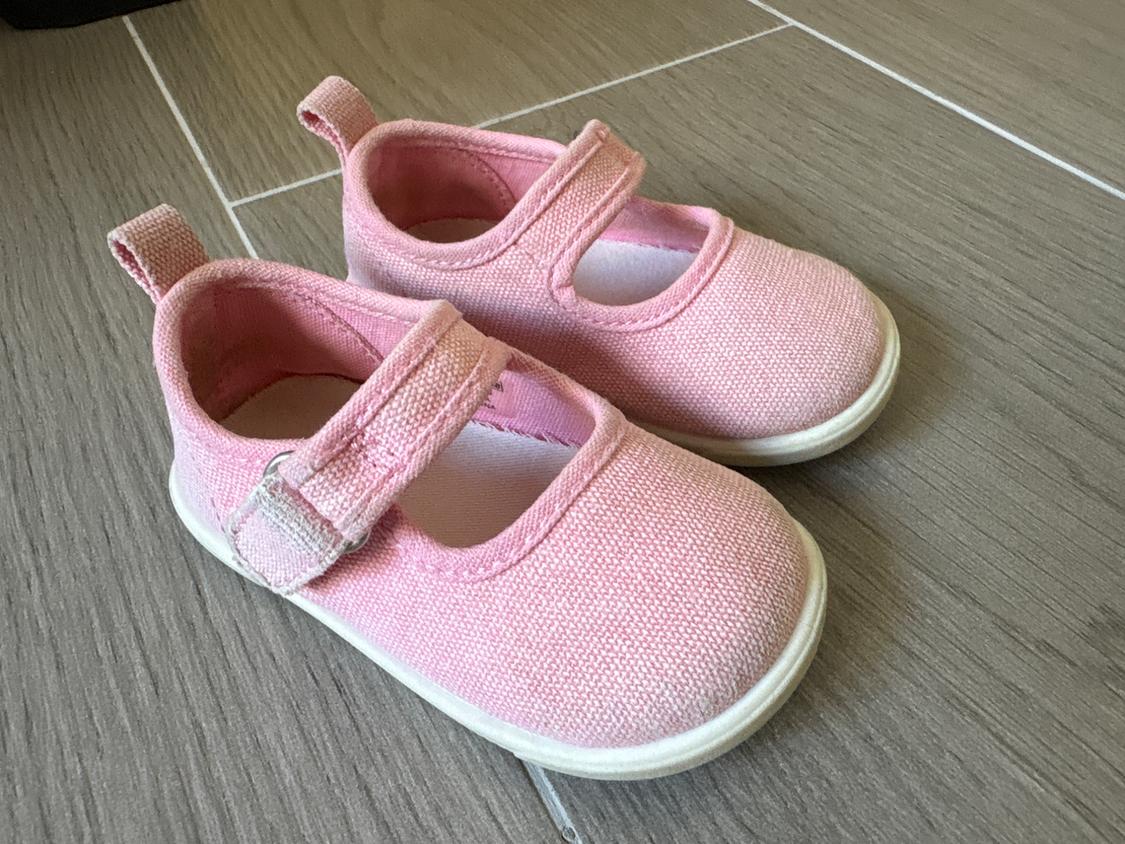 Pink children's footwear with hook-and-loop fastening on a brown tiled floor.