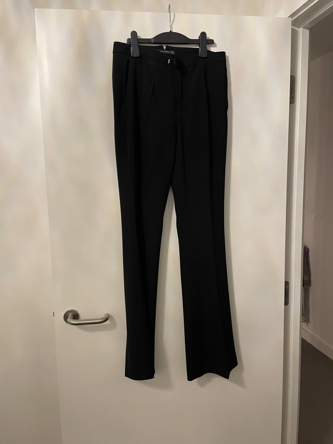 Black dress trousers hanging on a hanger on a white interior door.
