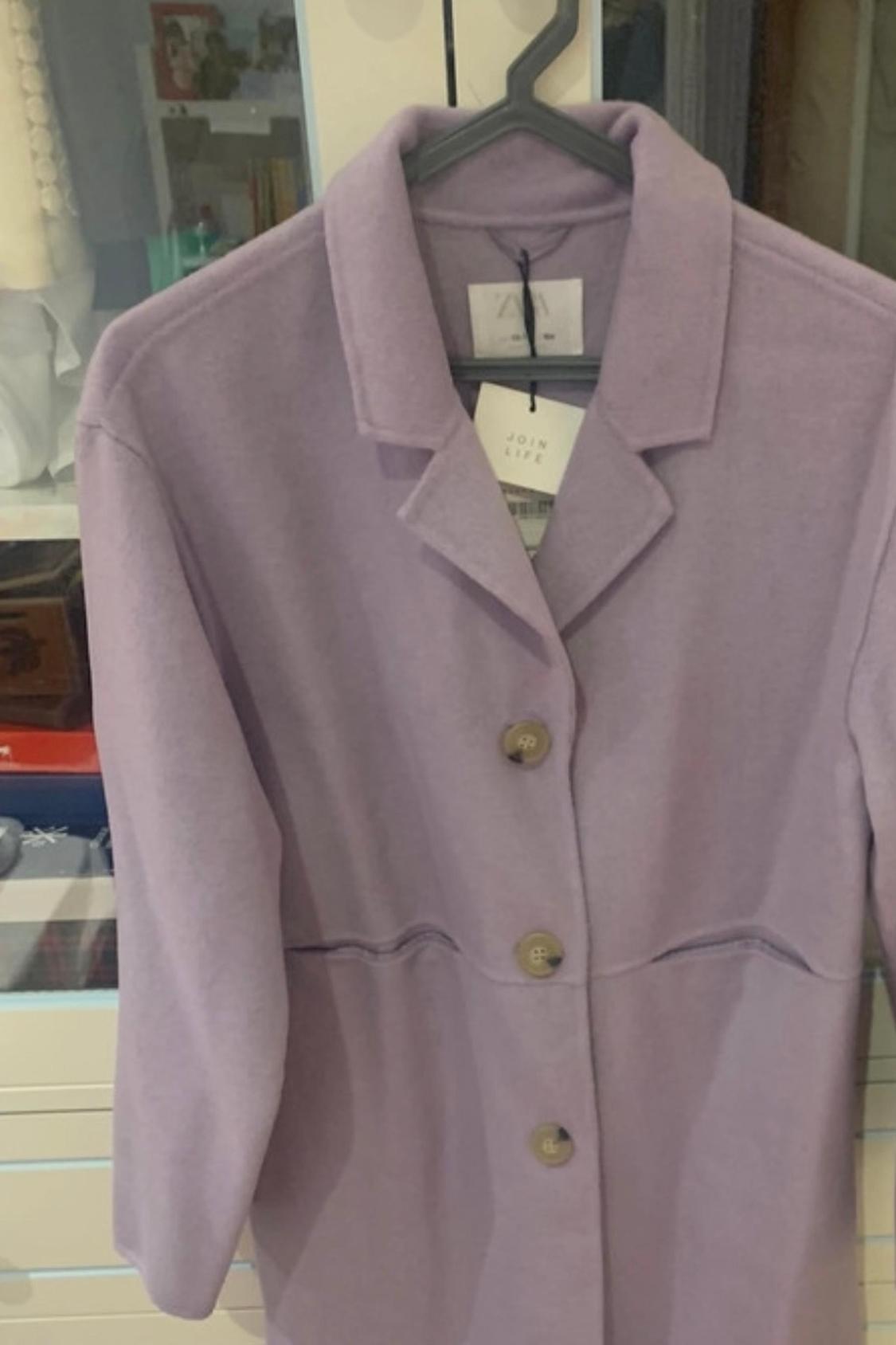 Medium shot of a lilac coat with visible buttons and a swing tag.