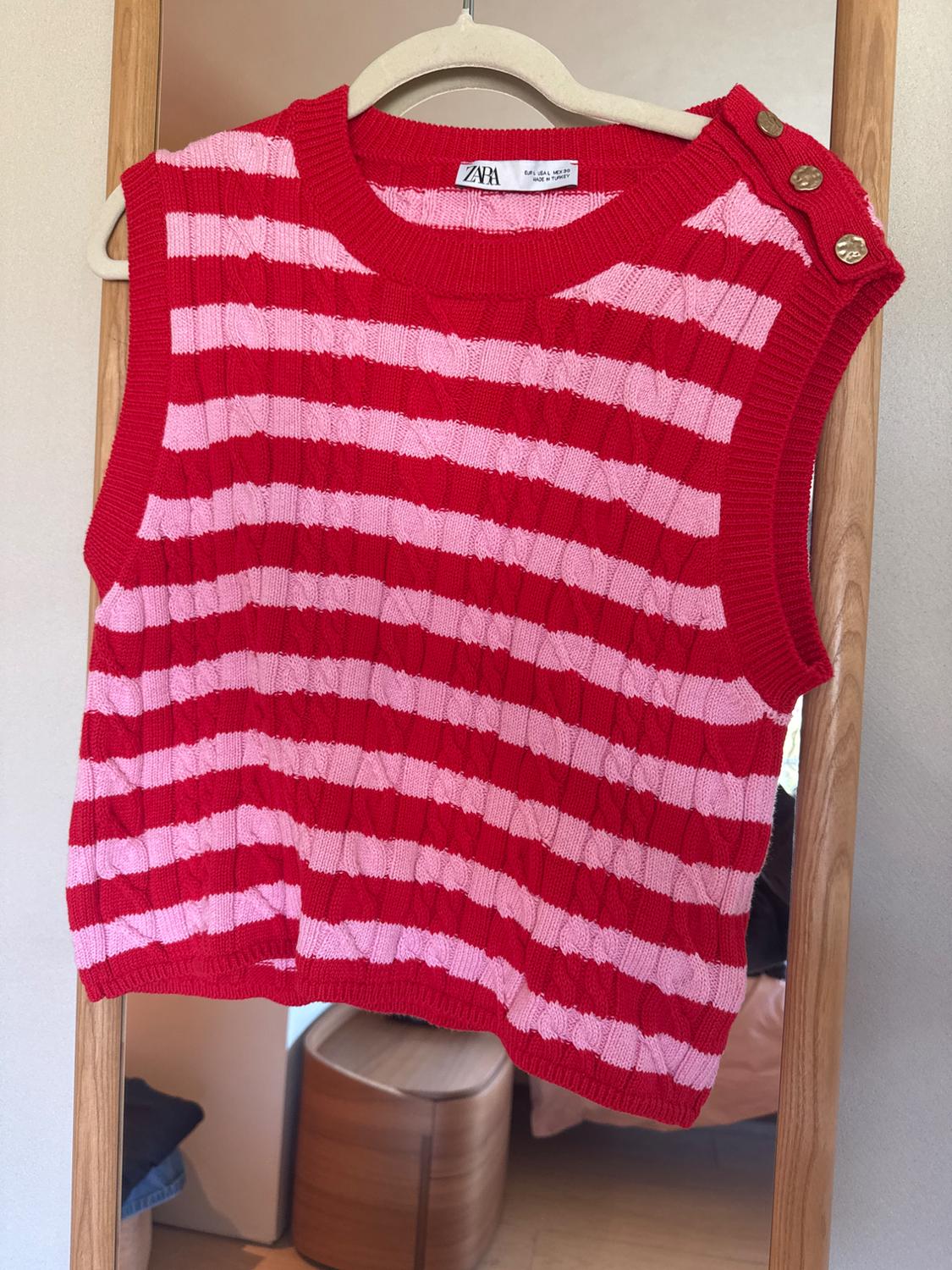 Red and pink striped waistcoat hanging on a wooden hanger. Detail of gold buttons on the shoulder. Visible label: Zara.