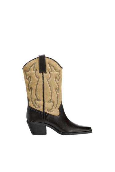 Black and beige leather cowboy boot with a decorative design on the side, a low heel, and a pointed toe on a white background.