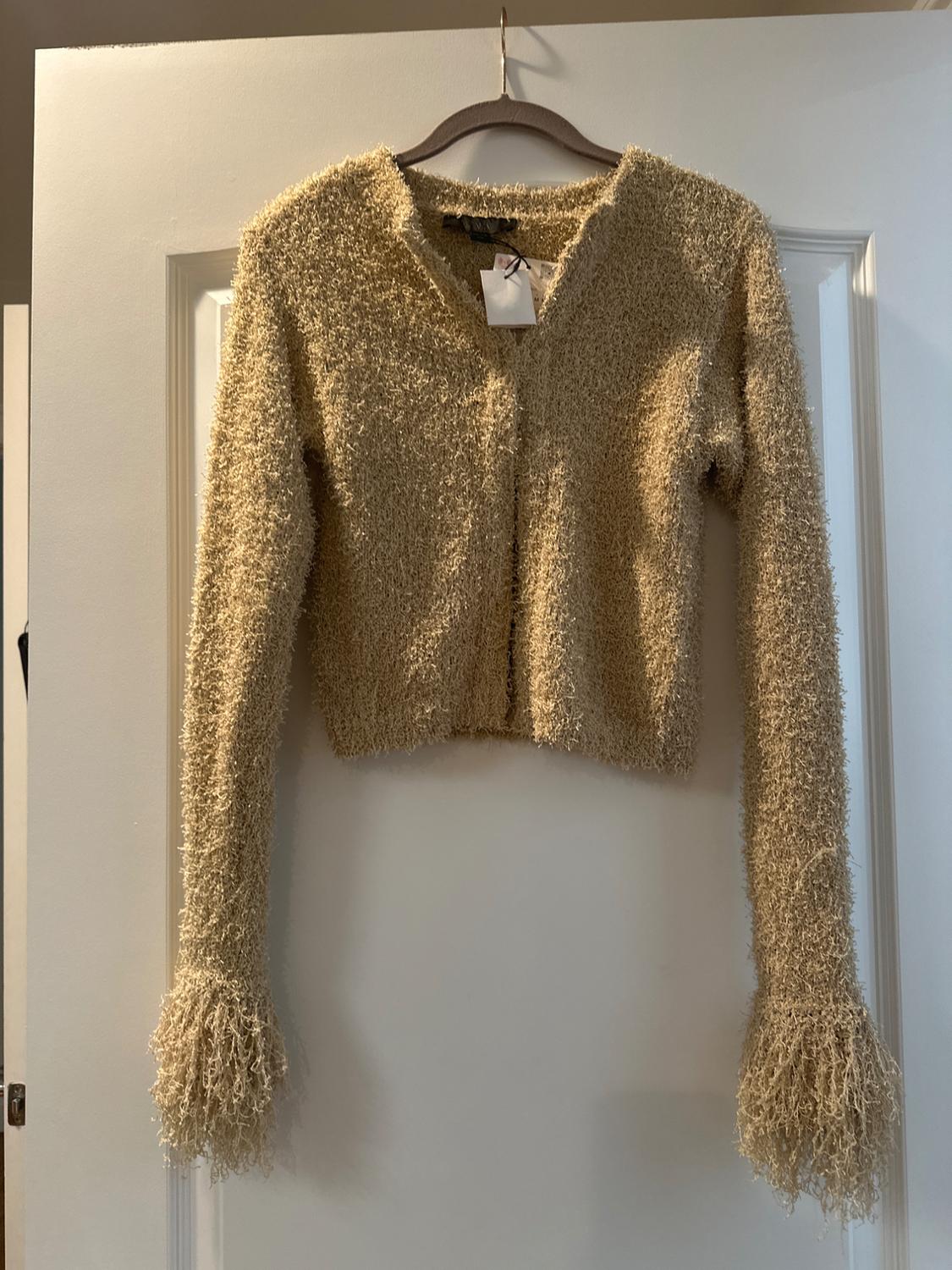 Beige knit jacket with a fuzzy texture, hanging on a wooden hanger over a white door. Label visible on the neck.