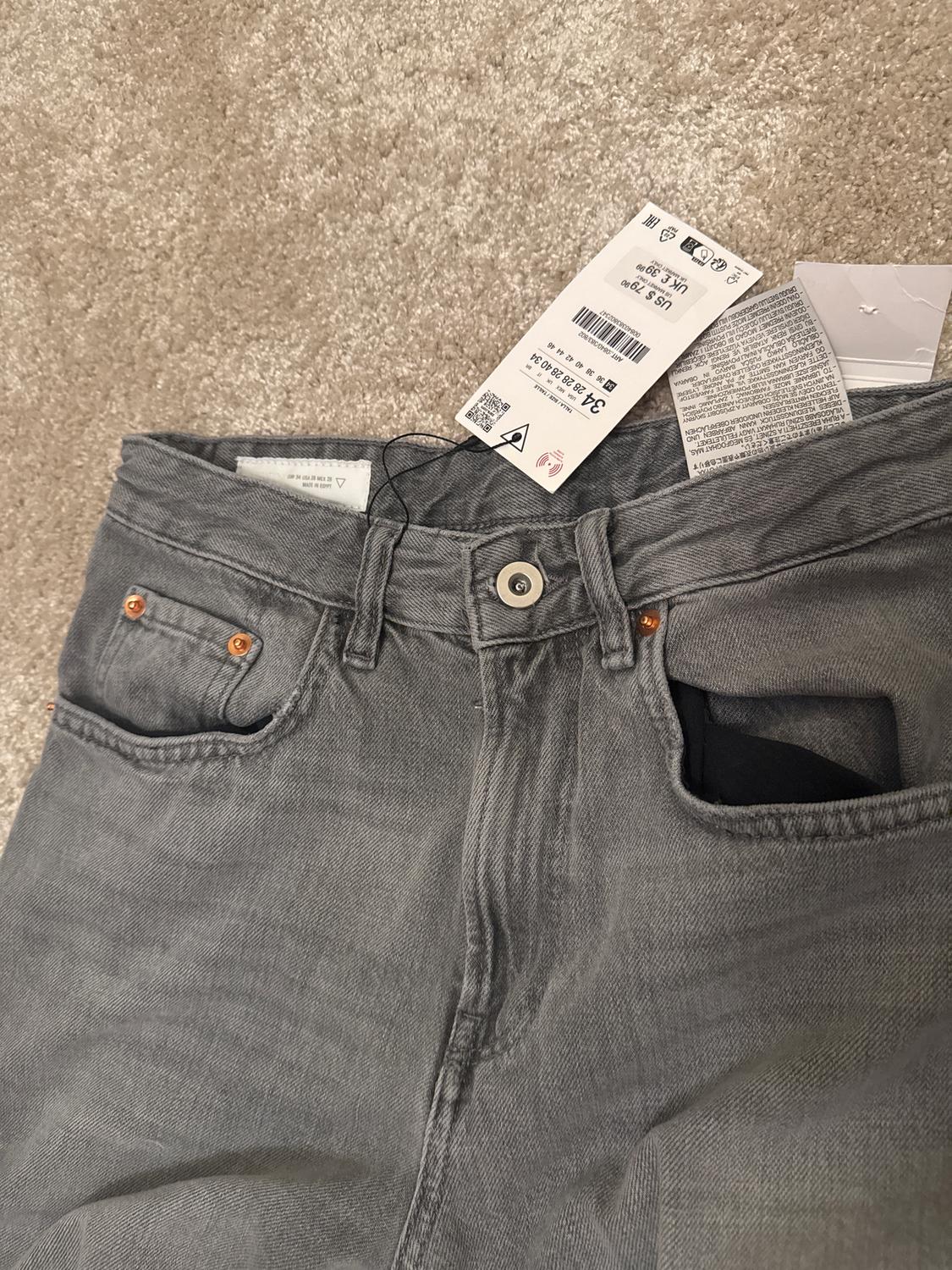 Grey jeans on a beige rug with visible labels on the waistband, showing size and care details.