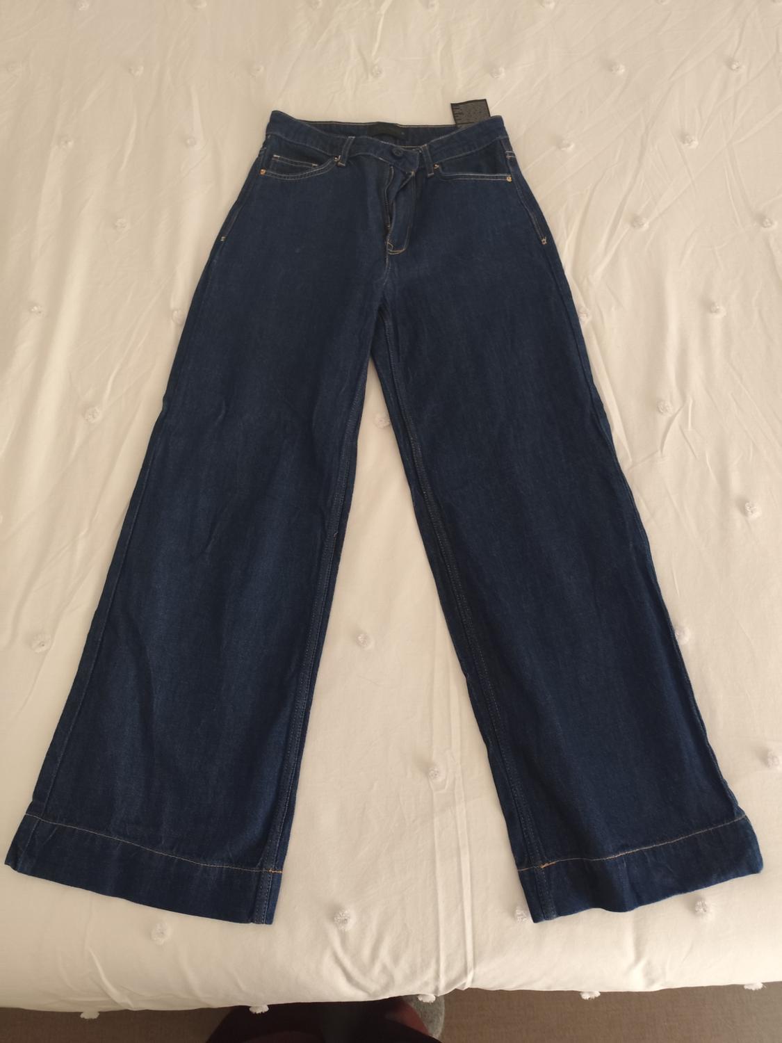 Dark blue, wide-leg denim trousers, placed on a white button-textured bedspread.