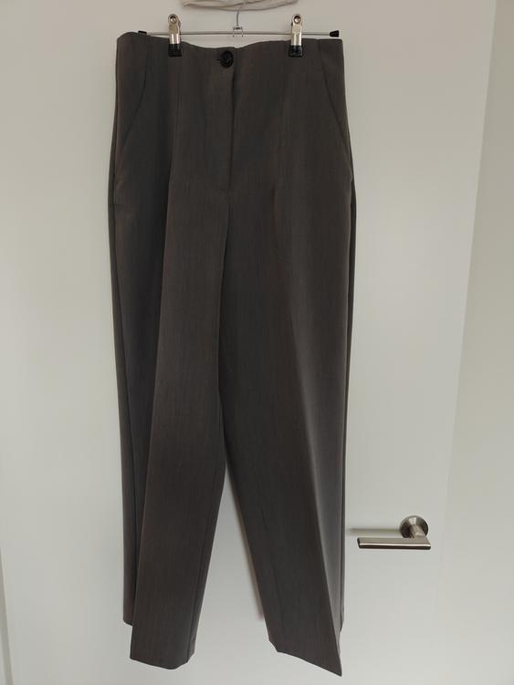 Grey dress trousers hanging on a hanger over a white door, with a black button visible at the top.