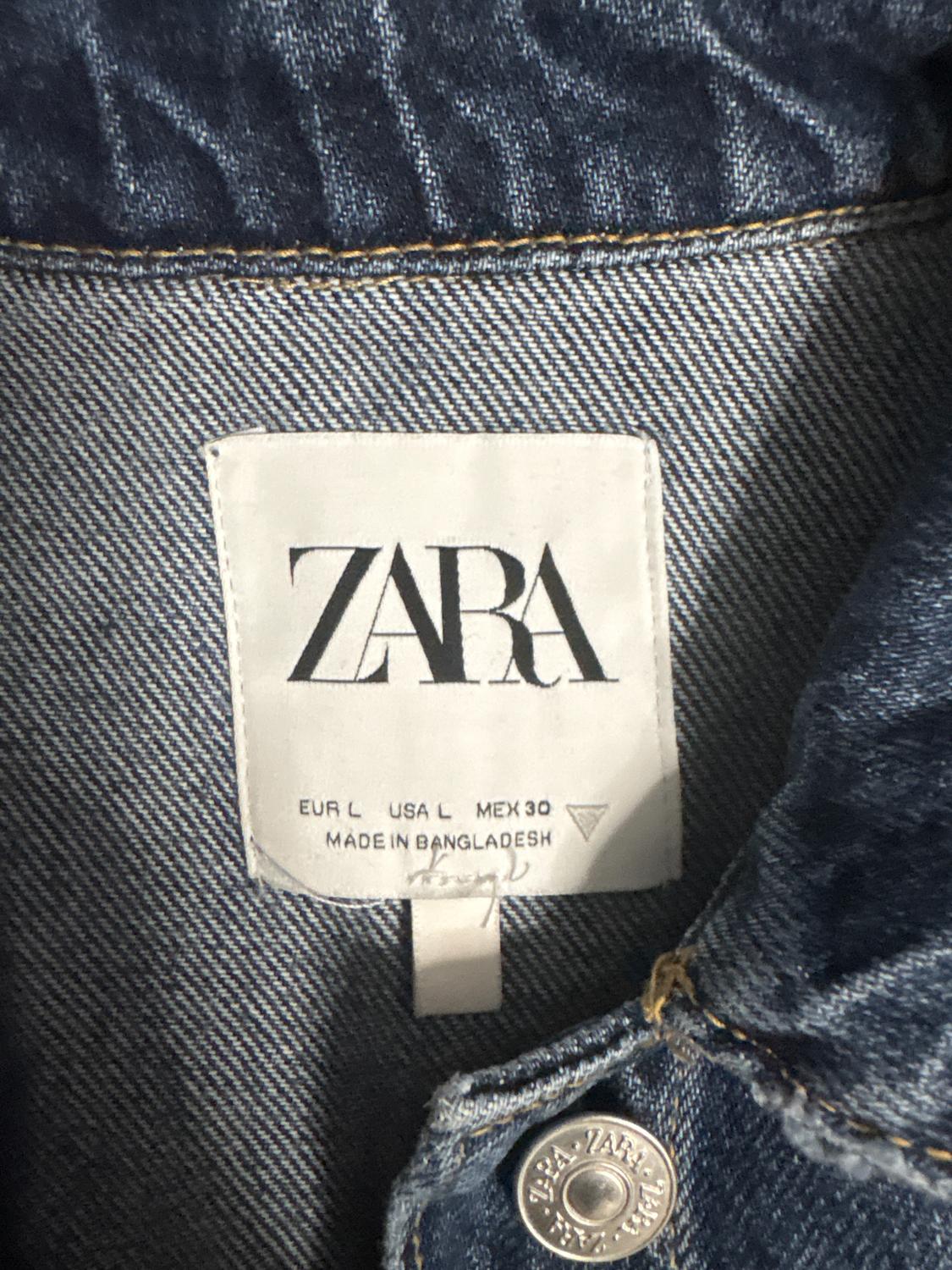ZARA denim jacket label. Text: EUR L USA L MEX 30 MADE IN BANGLADESH. Visible metal button with ZARA engraving.