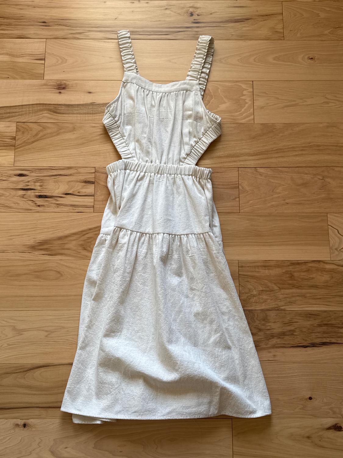 Sleeveless white dress with gathered straps, elastic waist, and a full skirt, on light hardwood flooring.