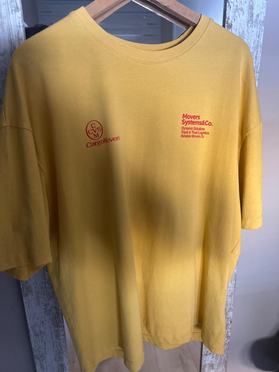 Yellow t-shirt hanging on a wooden hanger. Red text: "CargoMovers" and "Movers Systems&Co. Dynamic Solutions Track & Trust Logistics Reliable Movers Co."